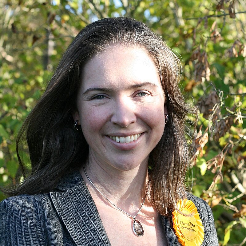 Anna in front of greenery wearing grey jacket with yellow rosset