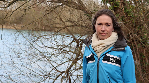 Anna in blue jacket standing in front of trees by a lake
