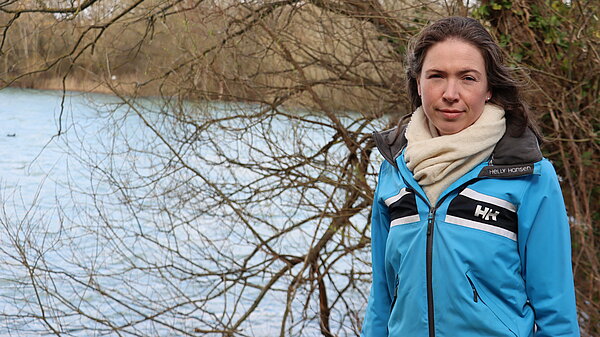 Anna in blue jacket standing in front of trees by a lake